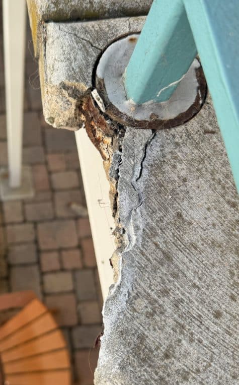 Broken concrete edge around a railing post before repair
