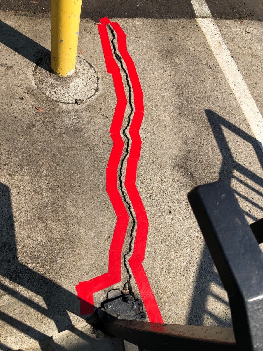 Open concrete crack marked with red tape before filling