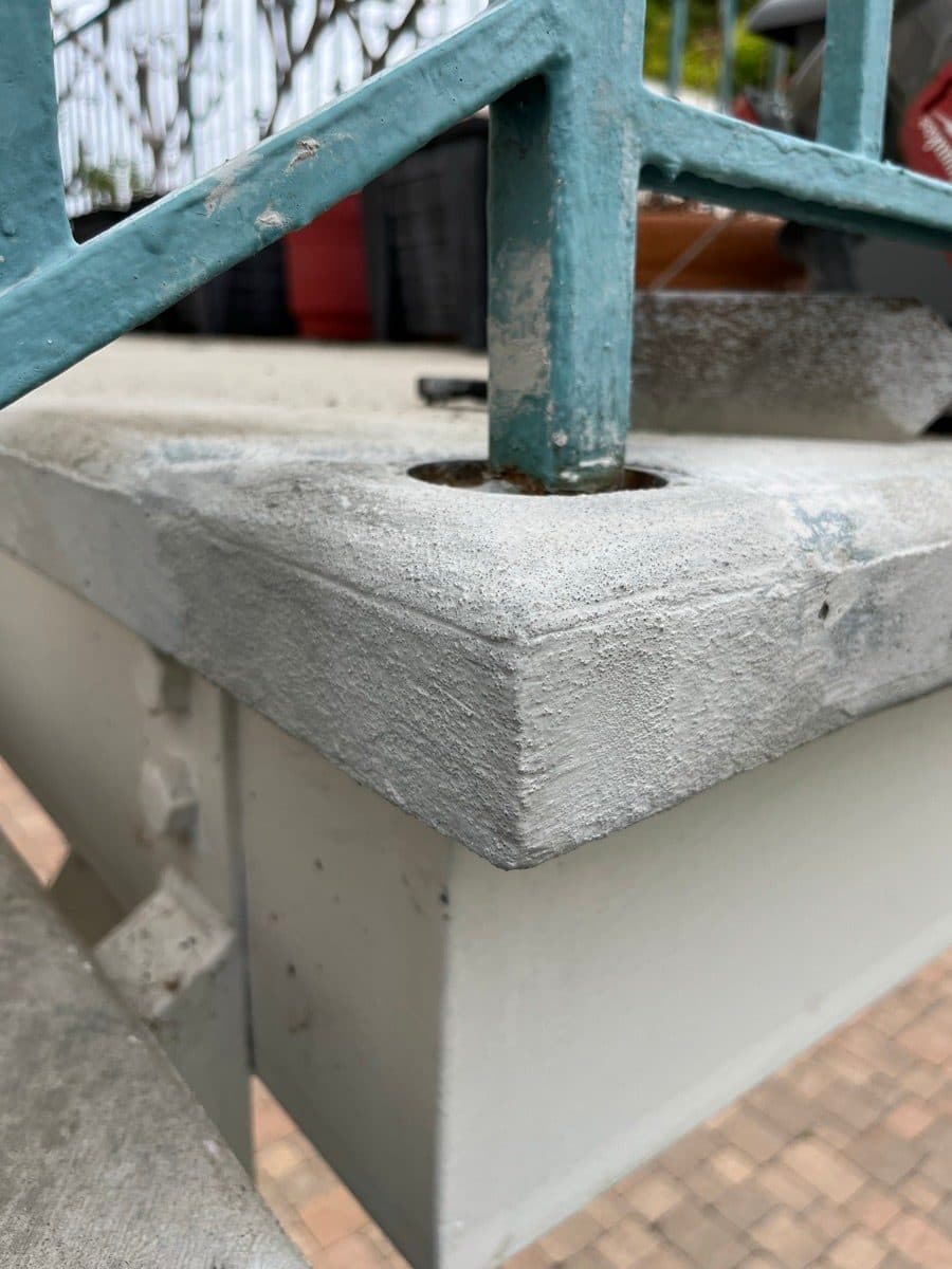 Repaired concrete corner around a blue railing post after patch work