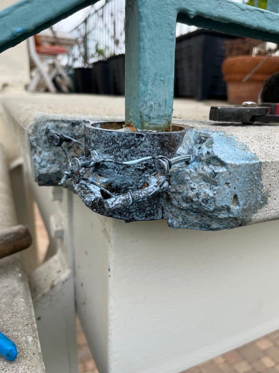 Damaged concrete corner around a blue railing post before repair