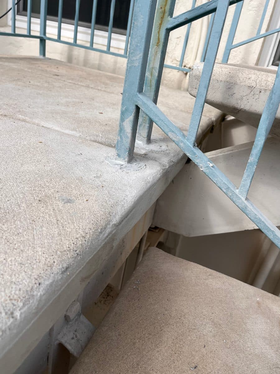 Patched concrete around blue railing posts after repair