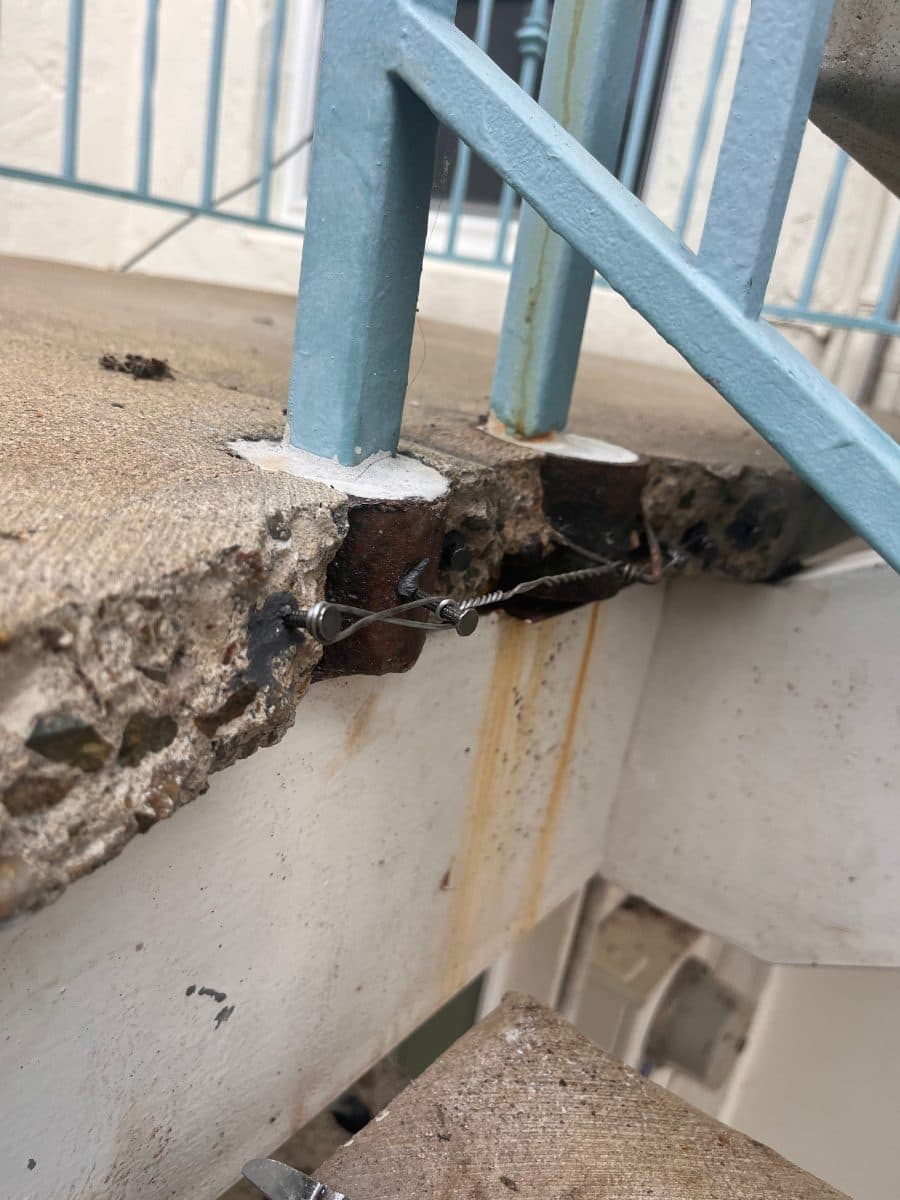 Spalled concrete around blue railing posts before repair